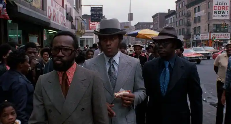 3 well dressed black men walk down a busy street in Black Cesar