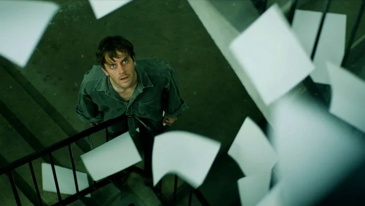 a man looks up at sheets of paper flapping around in the air