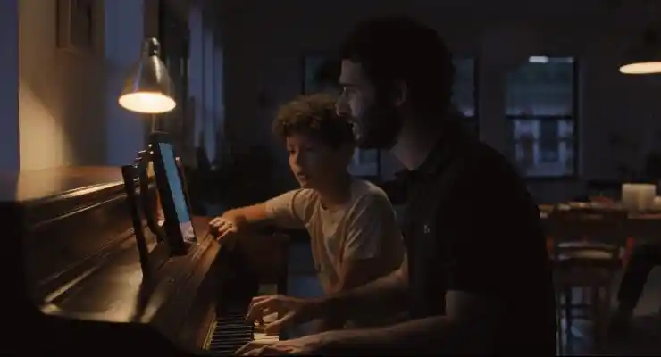 A man sits with a young boy at a piano in CLub Kid
