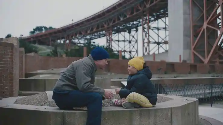 A man sits with his daughter next to a bridge in Josephine